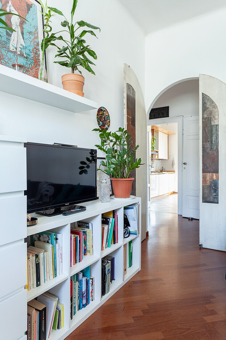 Wohnzimmer mit weißem Regal, Büchern und Topfpflanzen