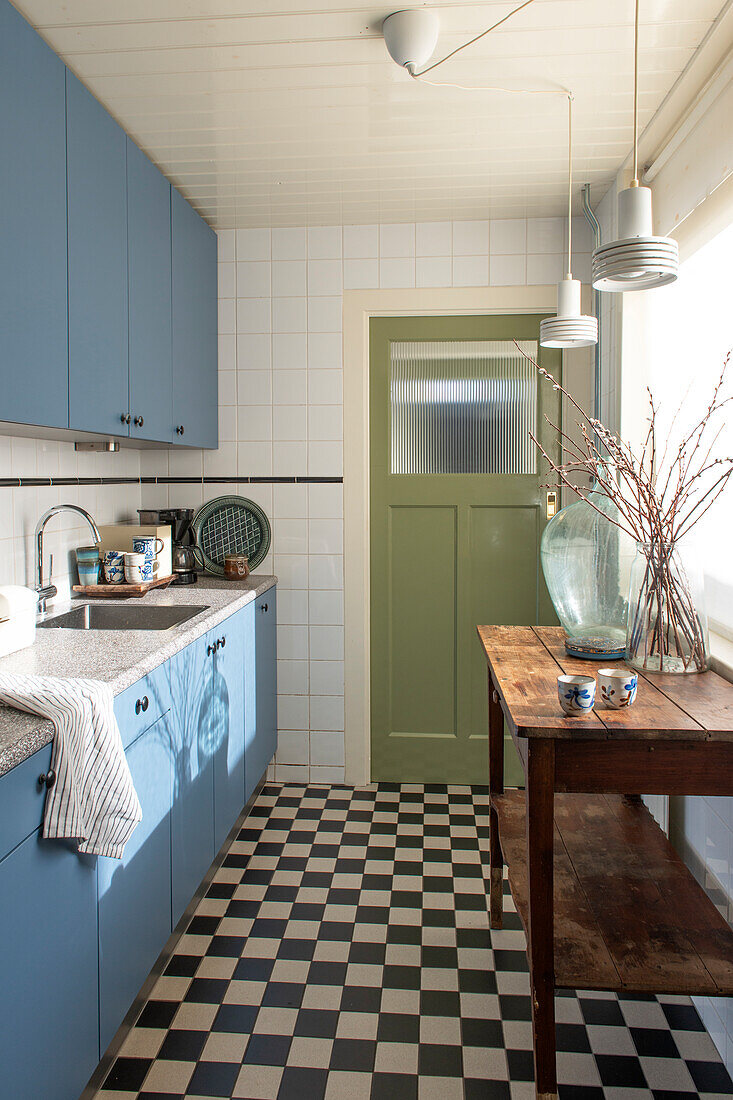 Kitchen with blue cabinets, black and white chequered floor and wooden table