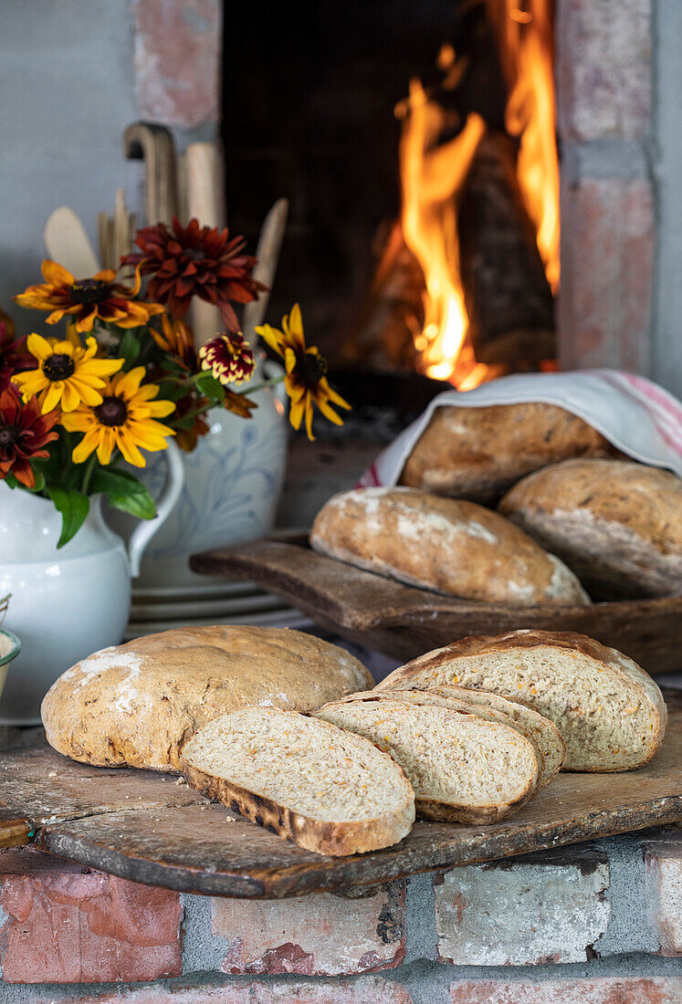 Frisch gebackenes Brot und Herbstblumen vor Kaminfeuer