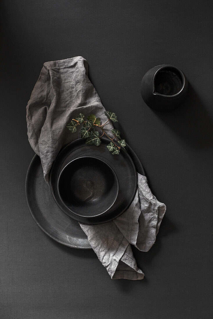Schwarze Keramikteller, Schale und Kanne auf schwarzem Untergrund