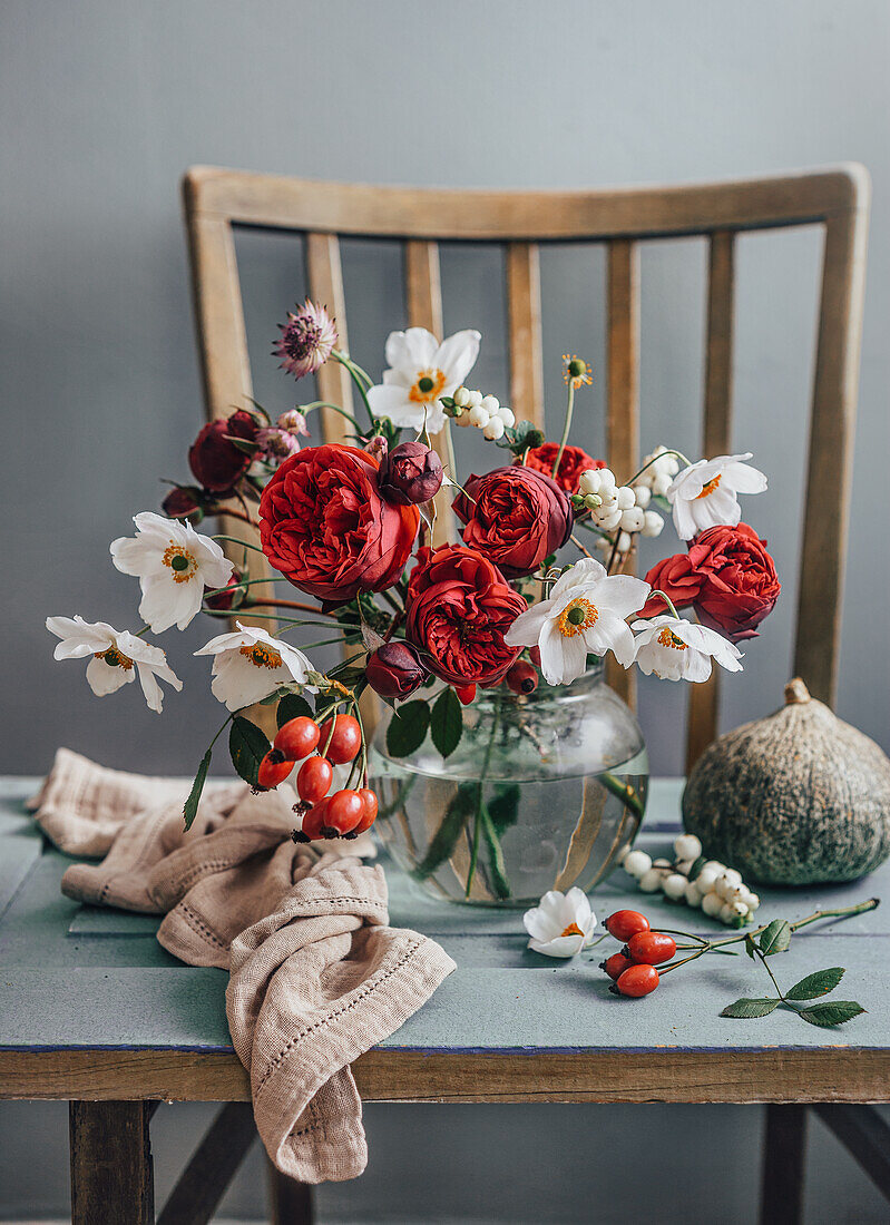 Blumenstrauß mit Rosen und Hagebutten in Glasvase