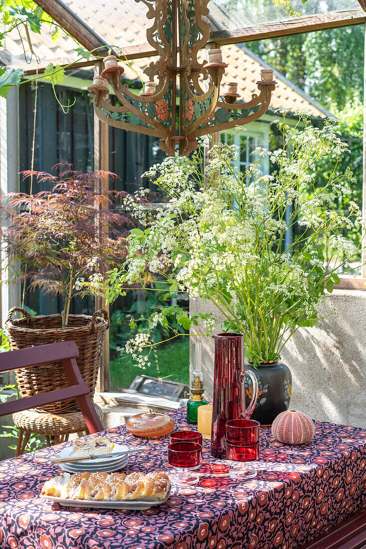 Gedeckter Tisch im Freien mit Sommerblumen, Überdachung aus Glas, rustikaler Kronleuchter