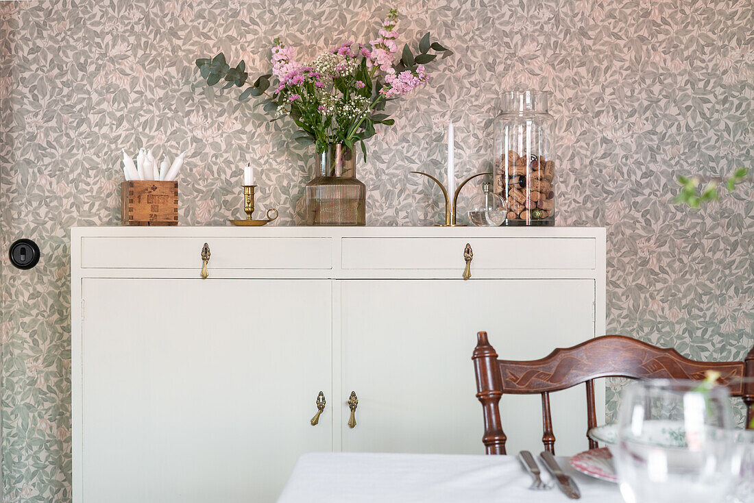 Bouquet of flowers on sideboard in front of patterned wallpaper in dining area