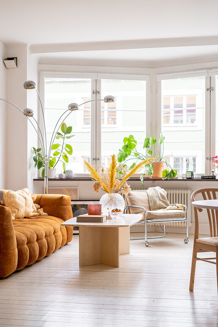 Helles Wohnzimmer mit Designersofa, Pflanzen auf Fensterbank und Bogenlampe