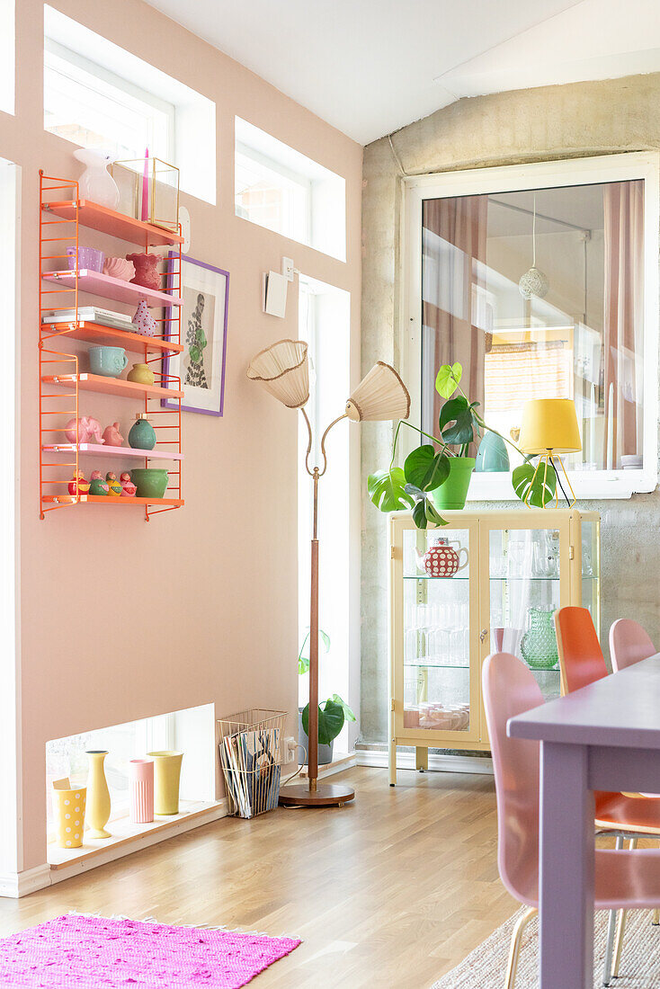 Colourful dining area with retro shelf and floor lamp in front of pink wall