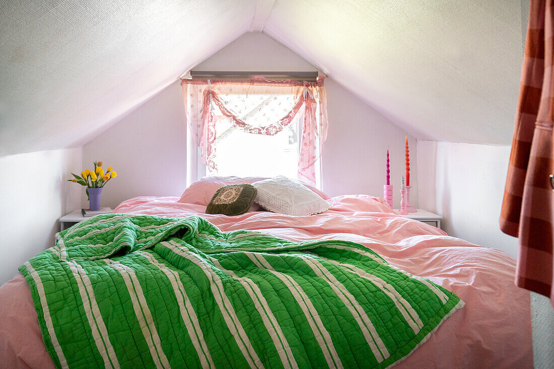 Schlafzimmer unterm Dach mit rosa Bettwäsche und grün-weiß gestreifter Decke