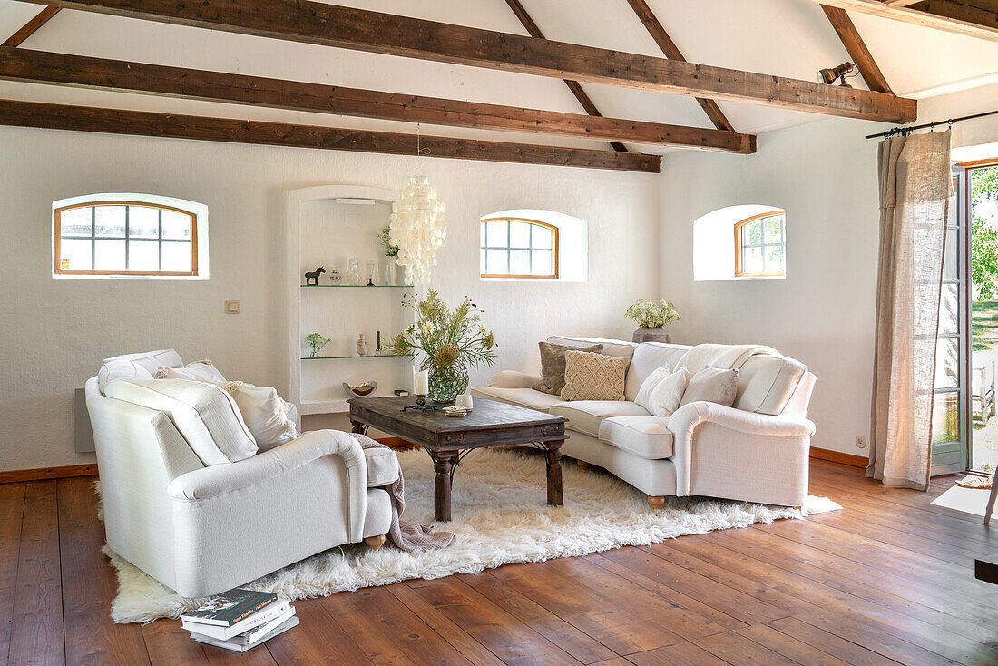 Bright living room with exposed beams, white sofas and wooden table