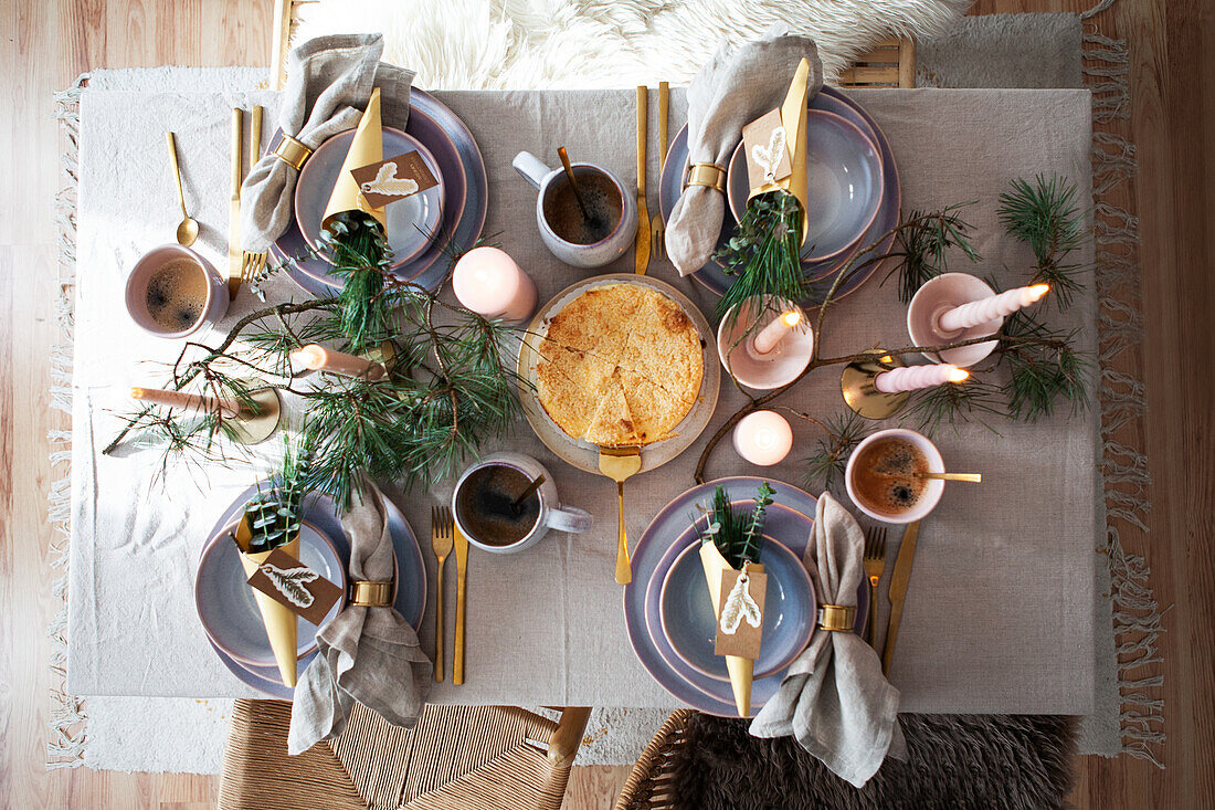 Festive dining table with gold-coloured cutlery and fir branches