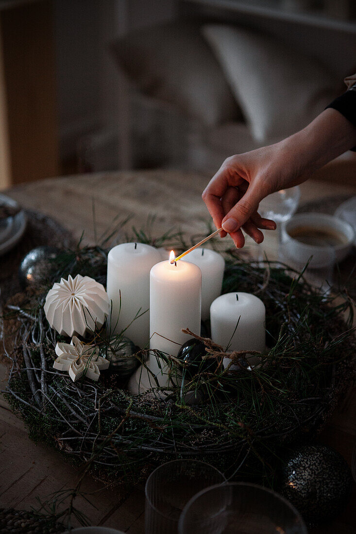 Hand entzündet weiße Kerze in einem Adventsgesteck