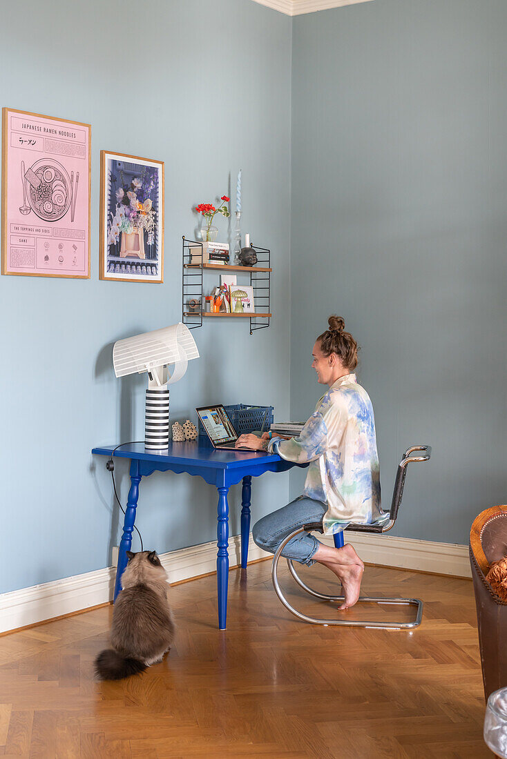 Frau arbeitet an blauem Schreibtisch im Homeoffice, Katze