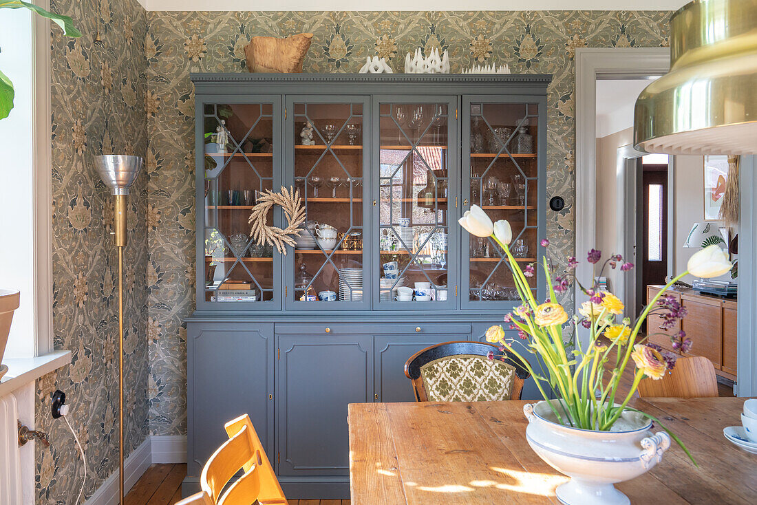 Dining room with display cabinet, patterned wallpaper and wooden table