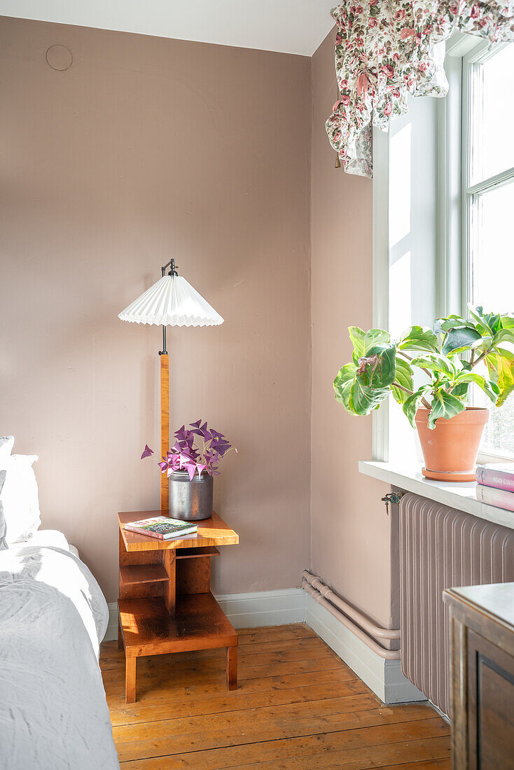 Wooden side table with lamp and houseplant on window sill in bedroom