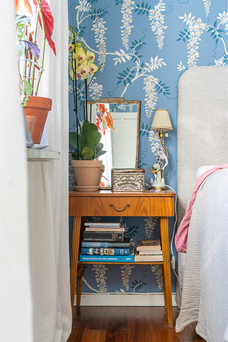 Vintage bedside table with books and table lamp next to bed