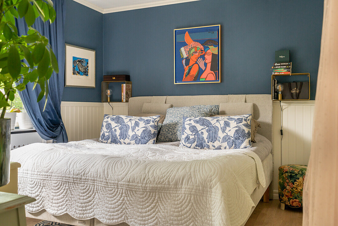 Doppelbett mit gemusterten Kissen im Schlafzimmer mit dunkelblauer Wand