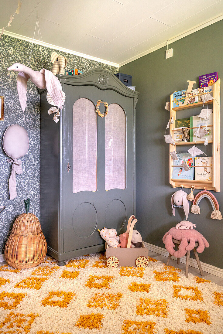 Children's room with vintage wardrobe in green, green walls, bookshelf, patterned wallpaper and fluffy carpet