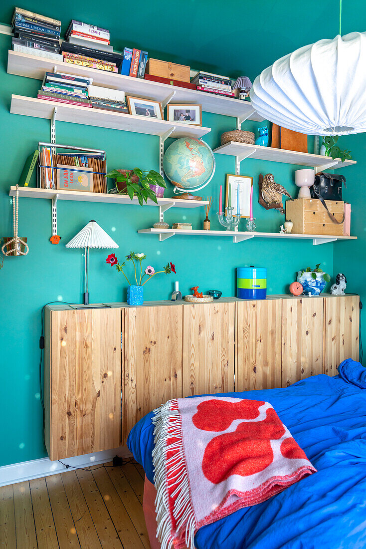 Open shelves, including narrow wooden cupboard in bedroom with blue wall
