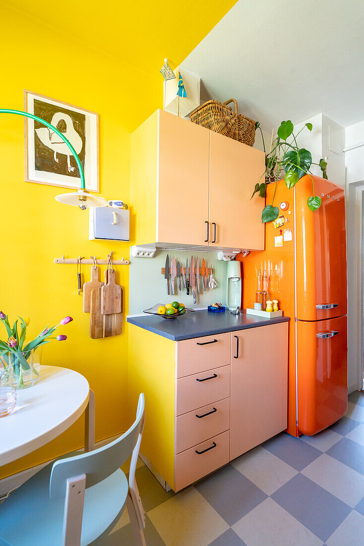 Orange-colored fridge and pink cupboards in kitchen with yellow wall