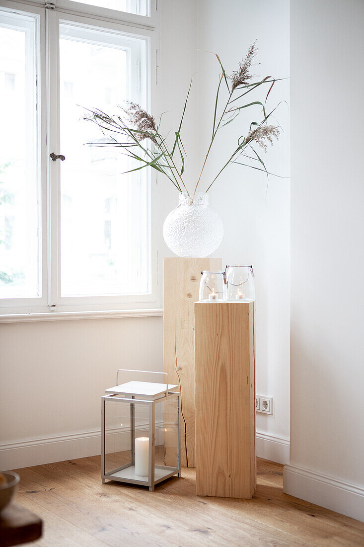 Vase with dried flowers on wooden pedestal next to glass lanterns