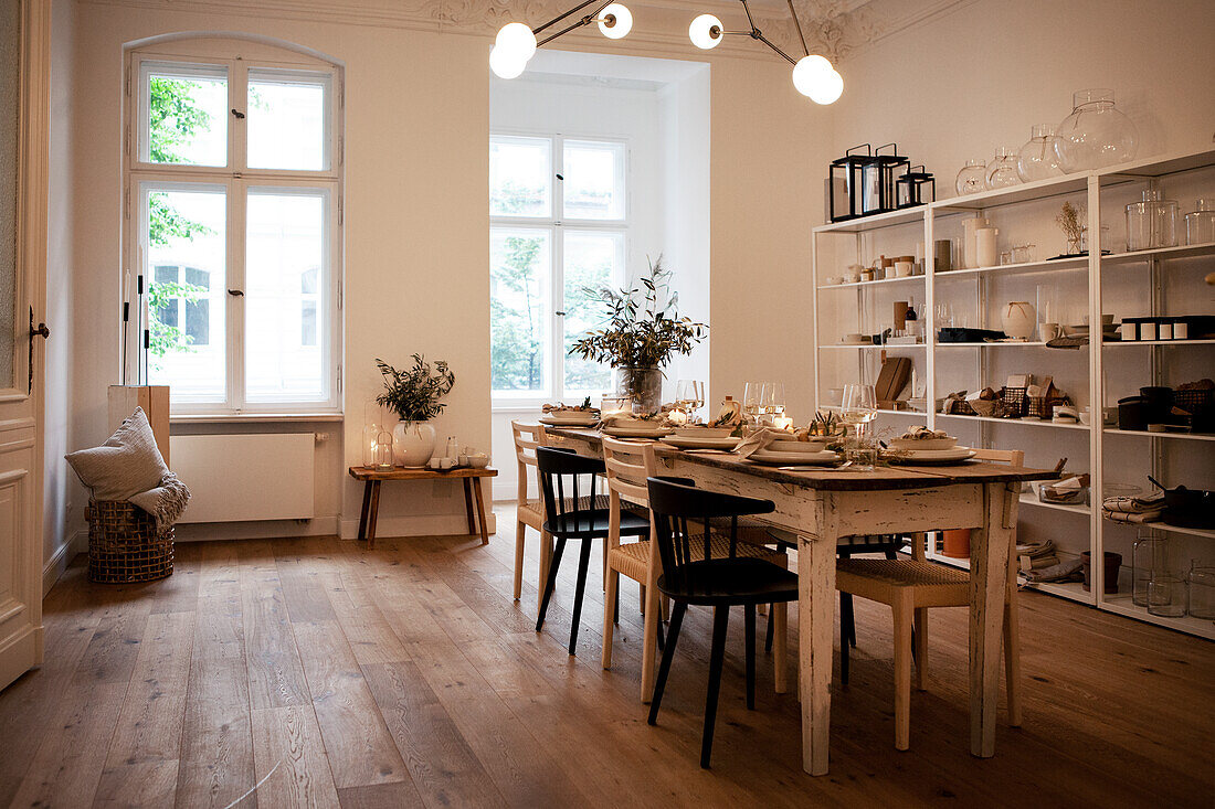 Dining area with wooden table and chairs in front of large windows and shelving wall