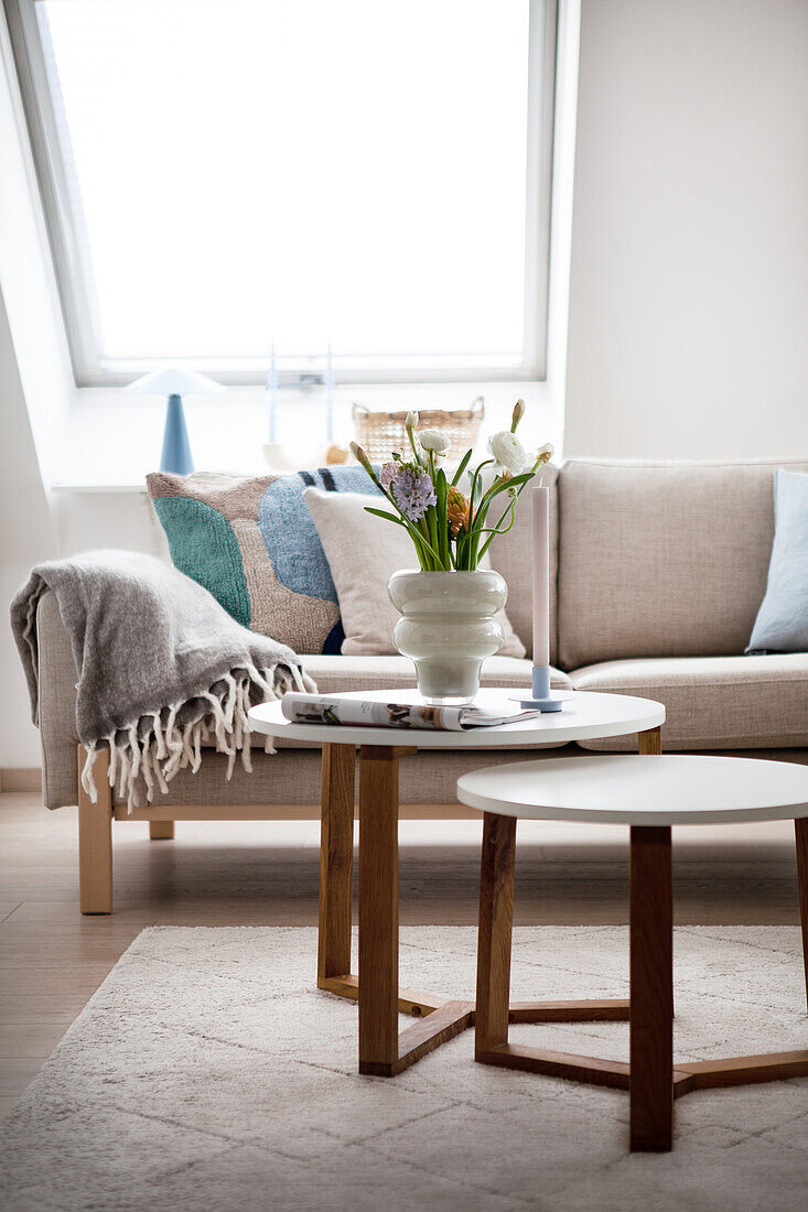 Bright living room with sofa, woollen blanket and round side tables