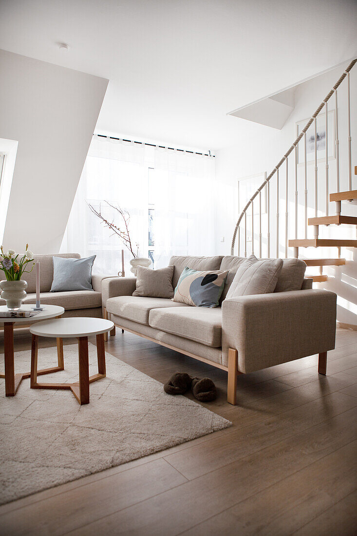 Bright living room with modern sofa, beige carpet and wooden staircase