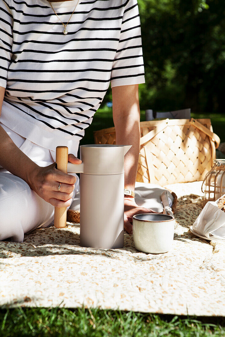 Picknick im Park mit Thermoskanne und Keramikbecher auf der Decke