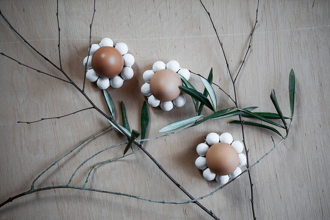 Eggs decorated as flowers on a wooden table with twigs and leaves