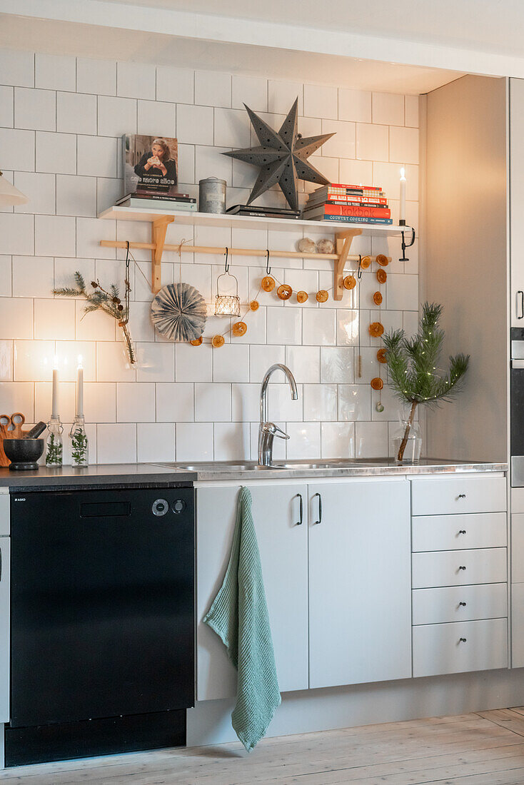 Kitchen decorated for Christmas with a star, dried oranges and fir branches, white tiled splashback