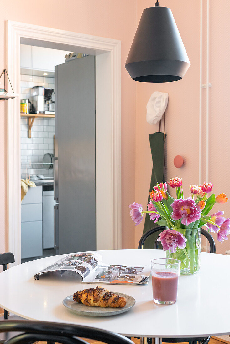 Esstisch mit Tulpenstrauß, Croissant, Zeitschrift und Getränk