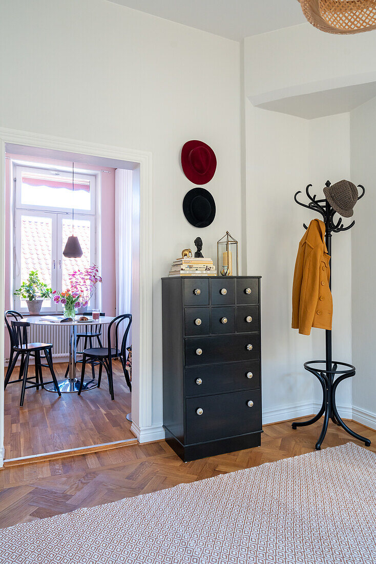 Hallway with herringbone parquet flooring, coat rack, black chest of drawers and carpet, view of dining area