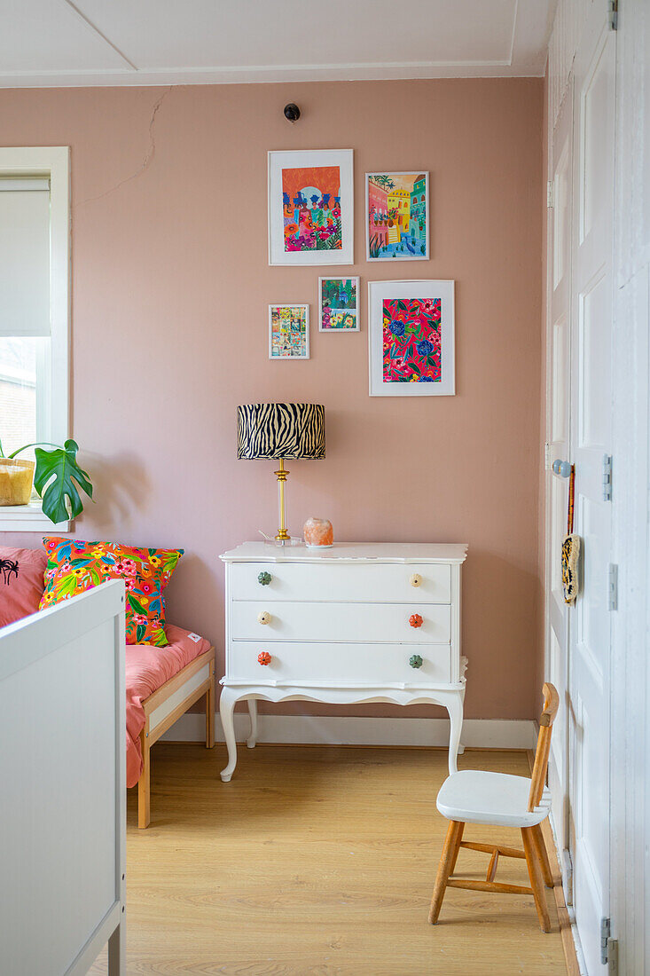 Vintage chest of drawers and colourful pictures on pink wall in bedroom