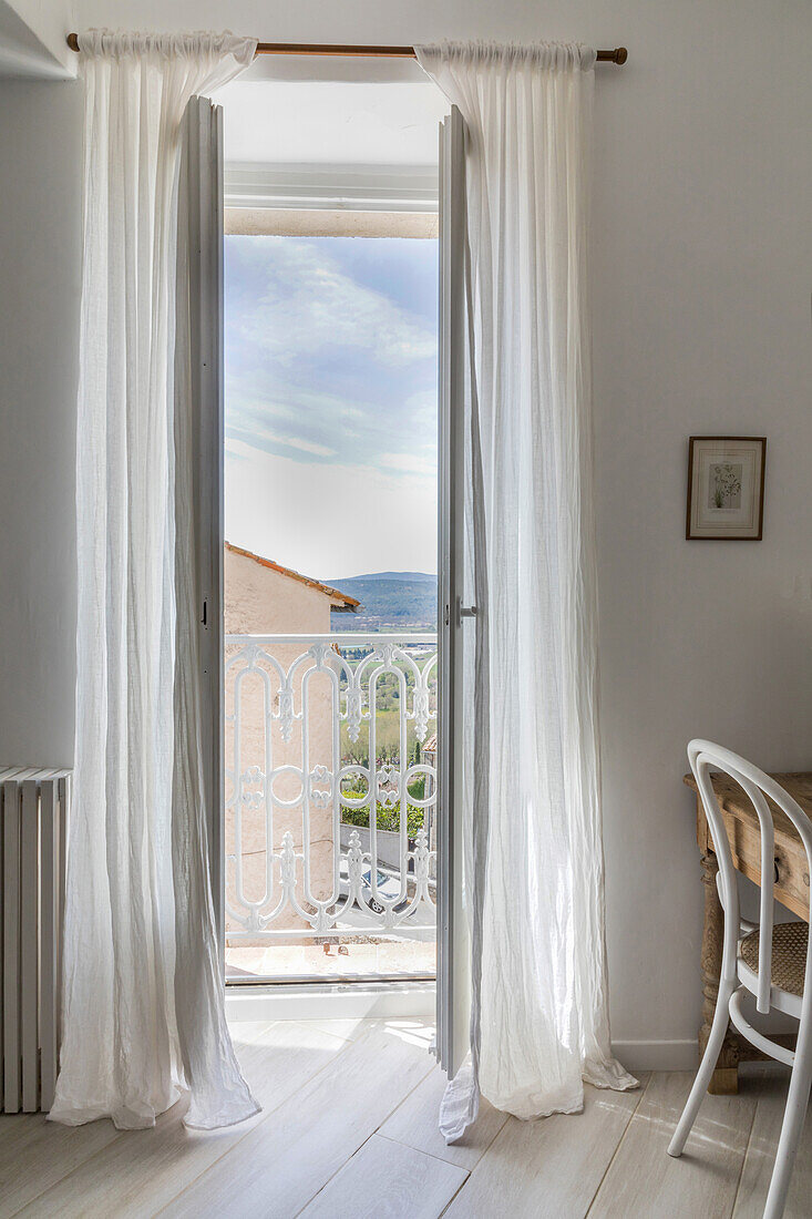 Blick durch bodenlange Vorhänge auf Balkon mit Geländer