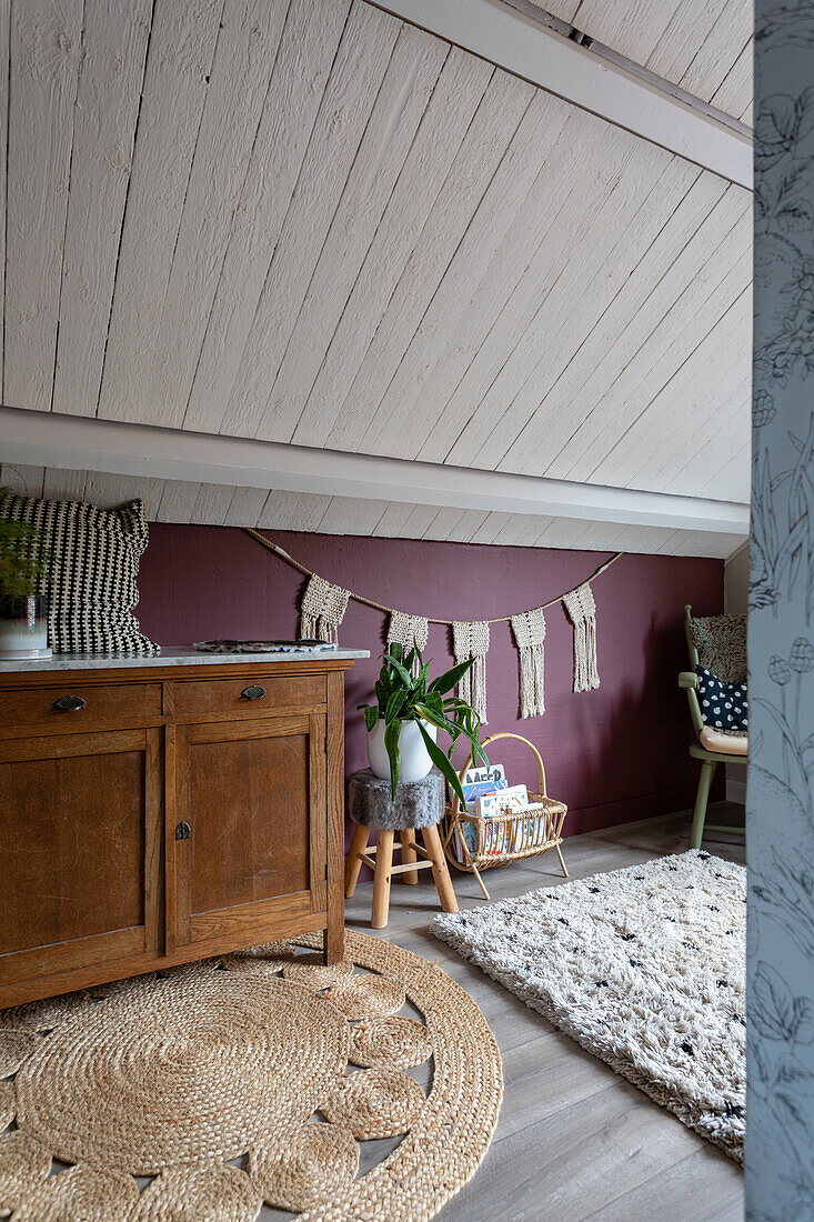 Children's room under a sloping roof with wooden furniture and bordeaux-coloured wall