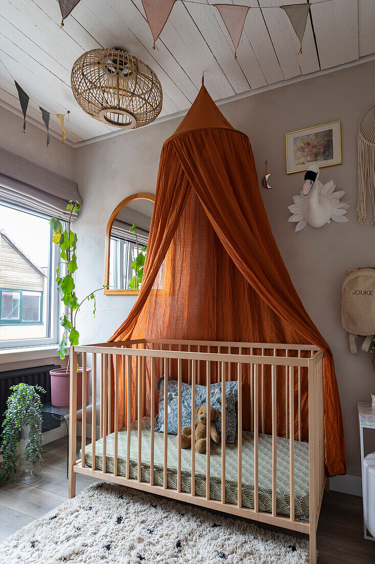 Children's bed with orange-coloured canopy and wall decoration in the children's room