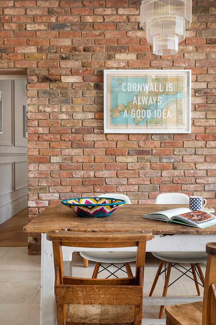 Rustic wooden table and chairs in front of brick wall with Cornwall poster