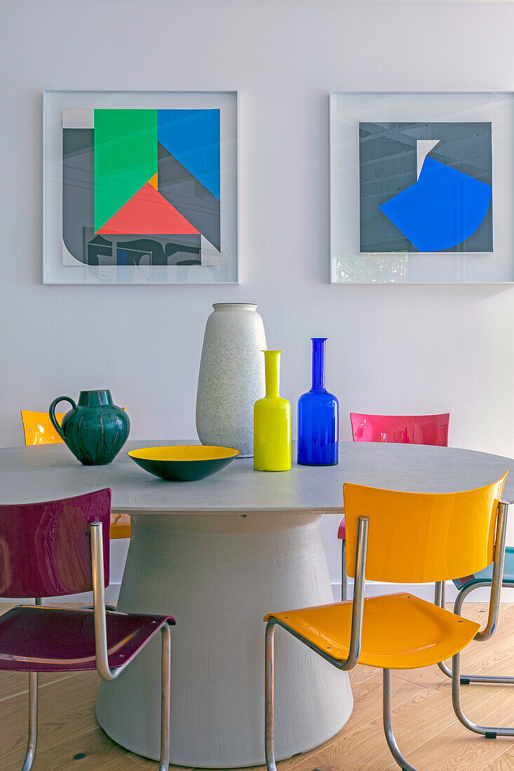 Oval dining table with colourful chairs, modern art on the wall above it