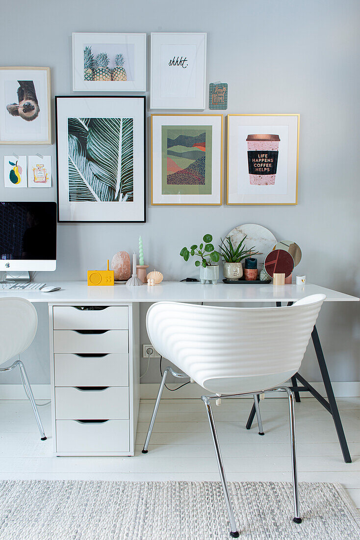 Modern gestalteter Arbeitsbereich mit vielen Bildern an der Wand, weißem Schreibtisch und weißen Stühlen