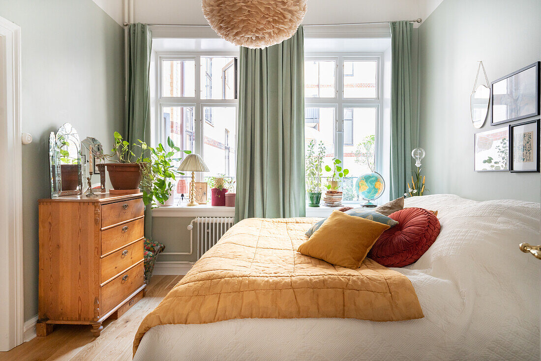 Gemütlich eingerichtetes Schlafzimmer mit grünen Vorhängen und Kommode aus Holz