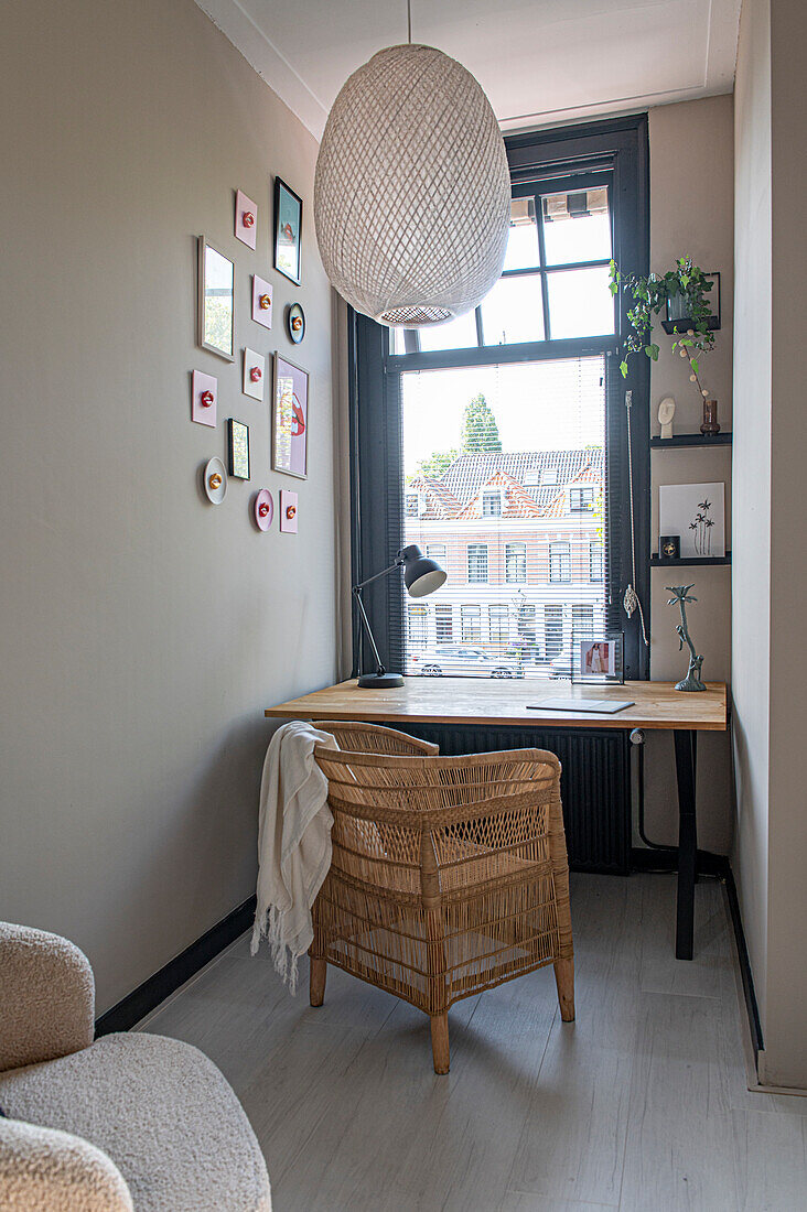 Schreibtisch und Rattansessel vor dem Fenster in schmalem Zimmer