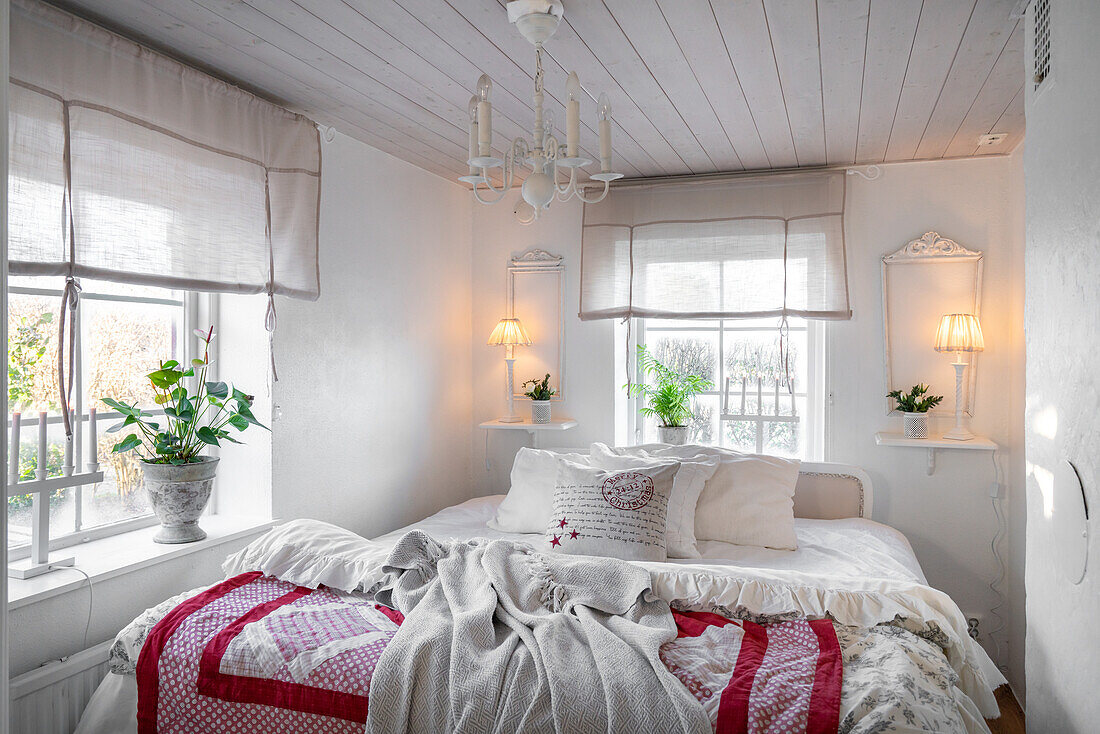 Brightly decorated bedroom with white wooden ceiling, chandelier and bed linen with red accents