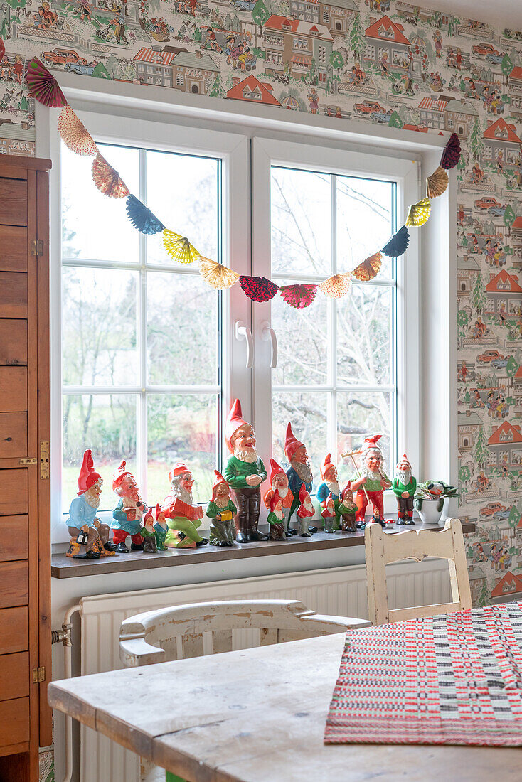 Garden gnome collection on a windowsill in the dining room with vintage wallpaper