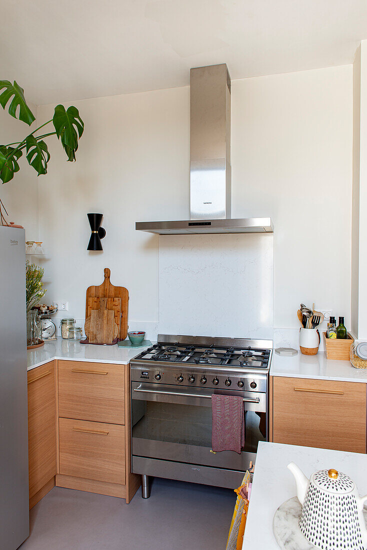 Moderne Küchenzeile aus hellem Holz und mit weißer Arbeitsplatte, Gasherd mit Dunstabzugshaube