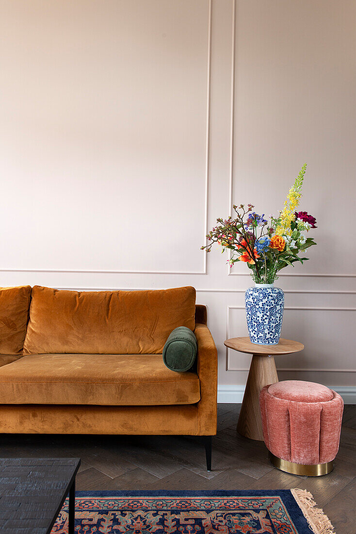 Orange-colored sofa, side table with bouquet of flowers and velvet-covered stool next to it