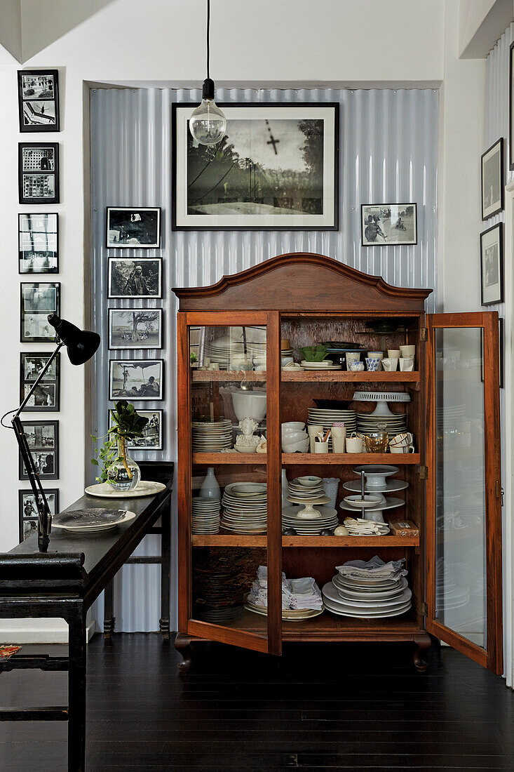 Antique crockery cupboard surrounded by black and white photo collection on corrugated plastic sheeting