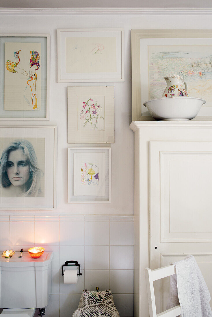 Watercolors and photos on white wall in bathroom