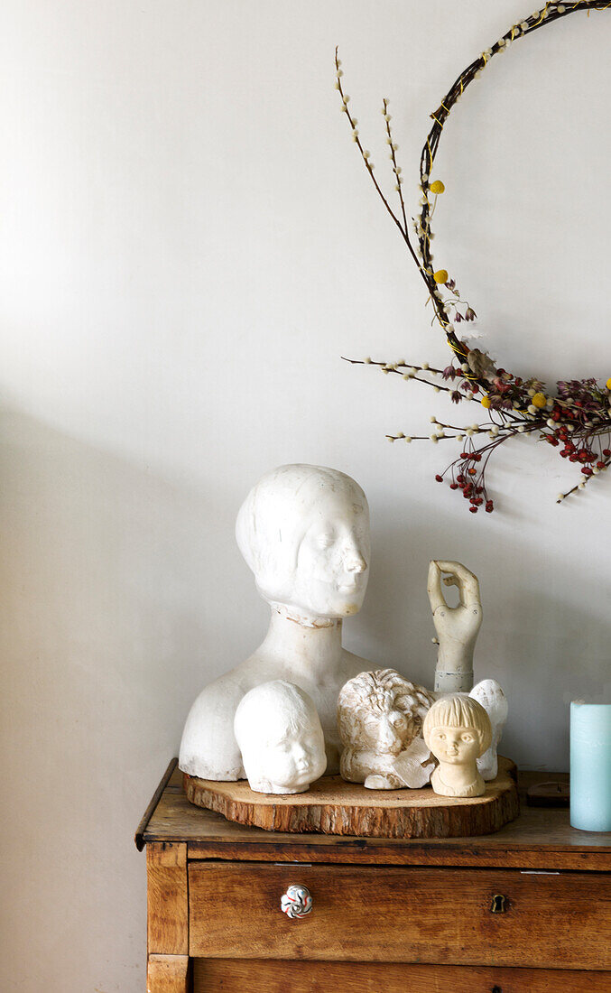Collection of busts on an old chest of drawers, with a wreath of dried flowers and berries above