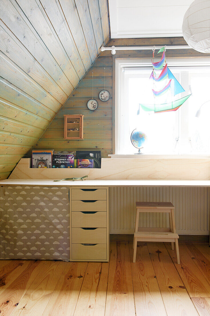 Long desk made of light-colored wood in front of the window in an attic room