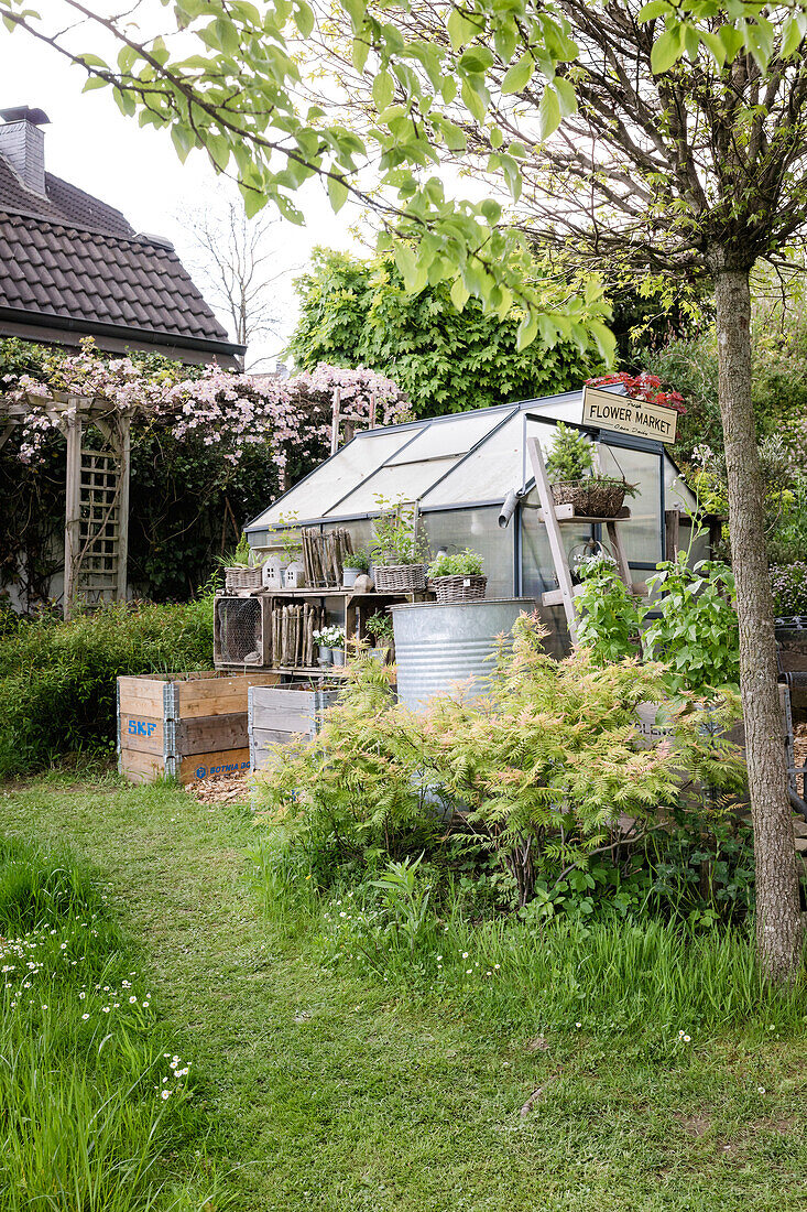 Kleines Gewächshaus mit "Flower Market"-Schild in einem Garten