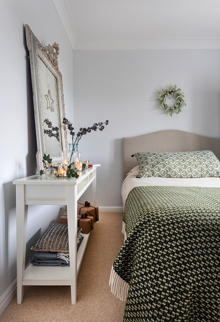White console with decoration next to bed with green bed linen in bedroom