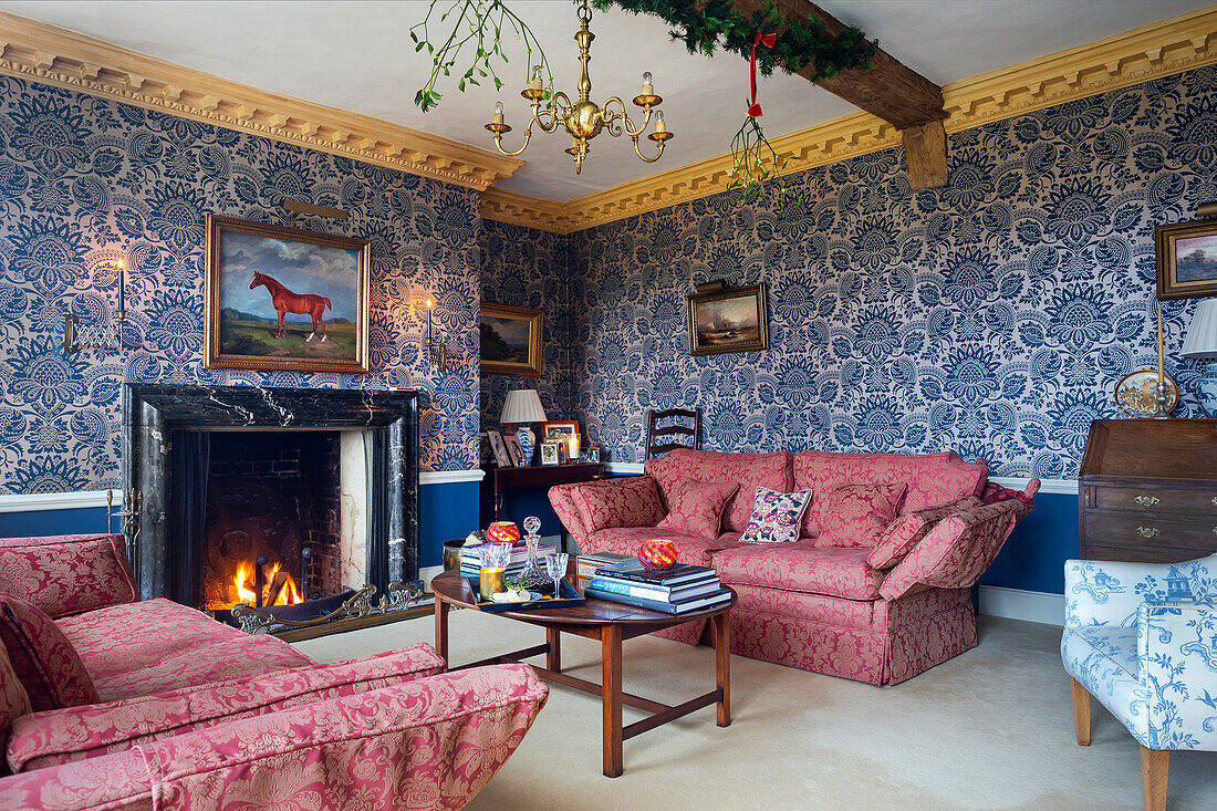 Traditionelles Wohnzimmer mit Kamin, roten Polstermöbeln und gemusterter Tapete